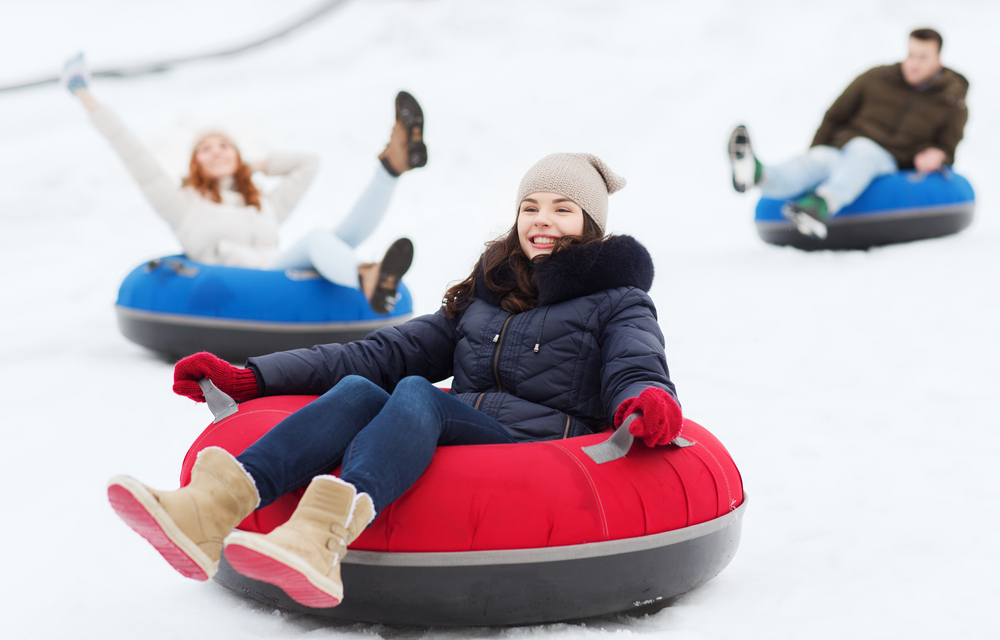 three people snow tubing down hill